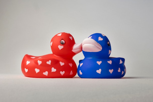 Love ducks with hearts on their bodies, whispering, kissing on cheek